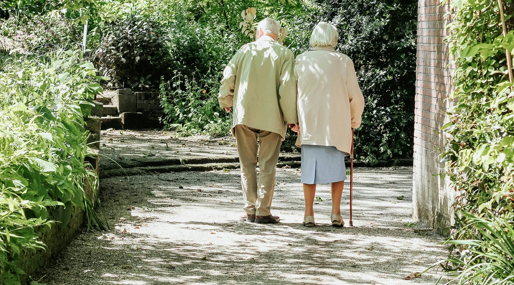 Ein älteres Paar geht Hand in Hand einen sonnigen Weg entlang